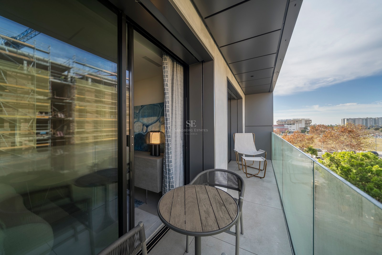 Balcon contemporain avec garde-corps en verre, table en bois et sièges donnant sur un parc.