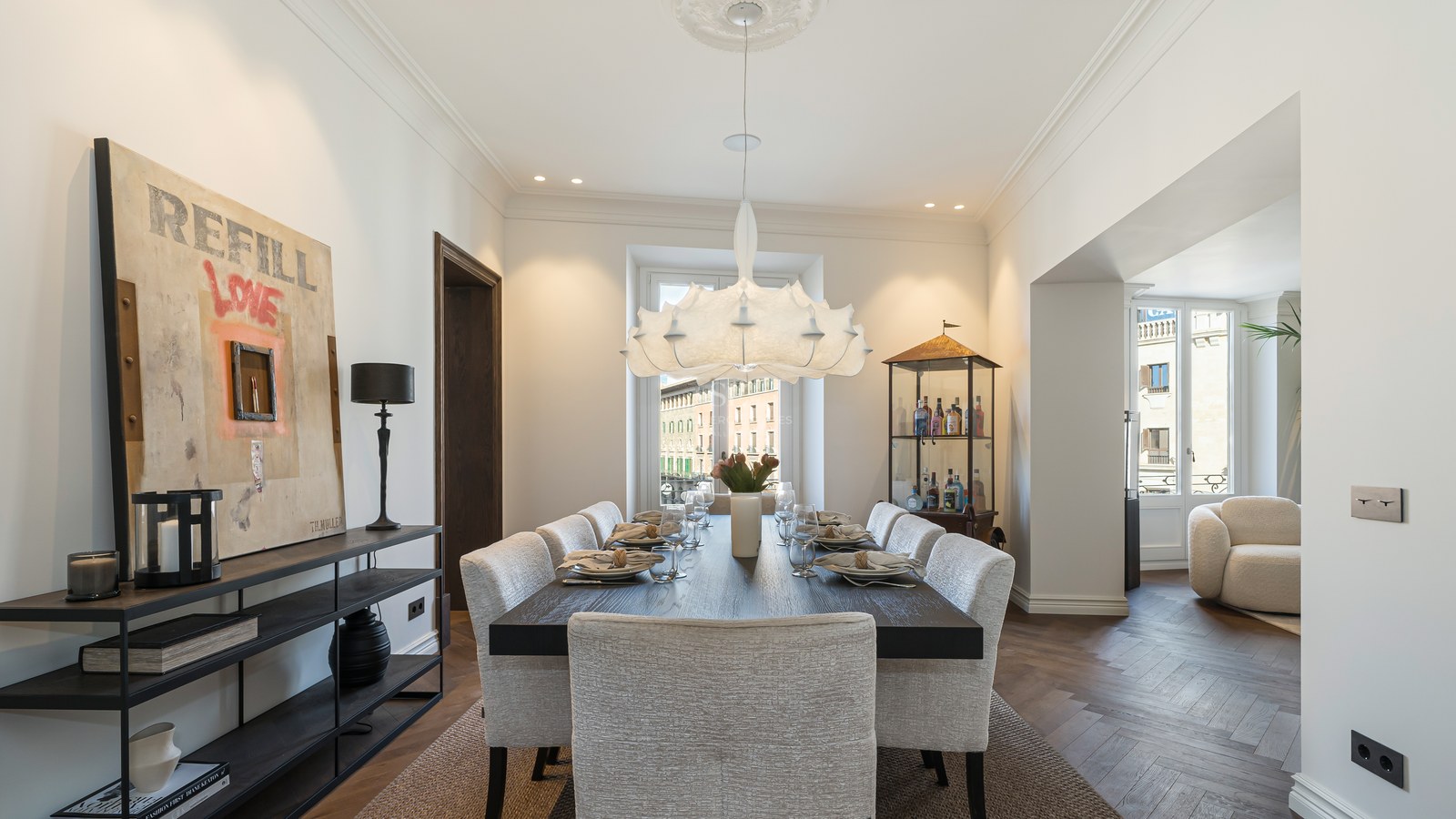 Comedor contemporáneo con mesa de madera oscura, sillas tapizadas, lámpara de diseño y suelos de roble en espiga.