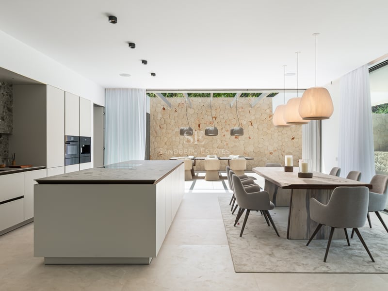 Cuisine contemporaine avec îlot en marbre et salle à manger s'ouvrant sur un patio ensoleillé avec mur en pierre.