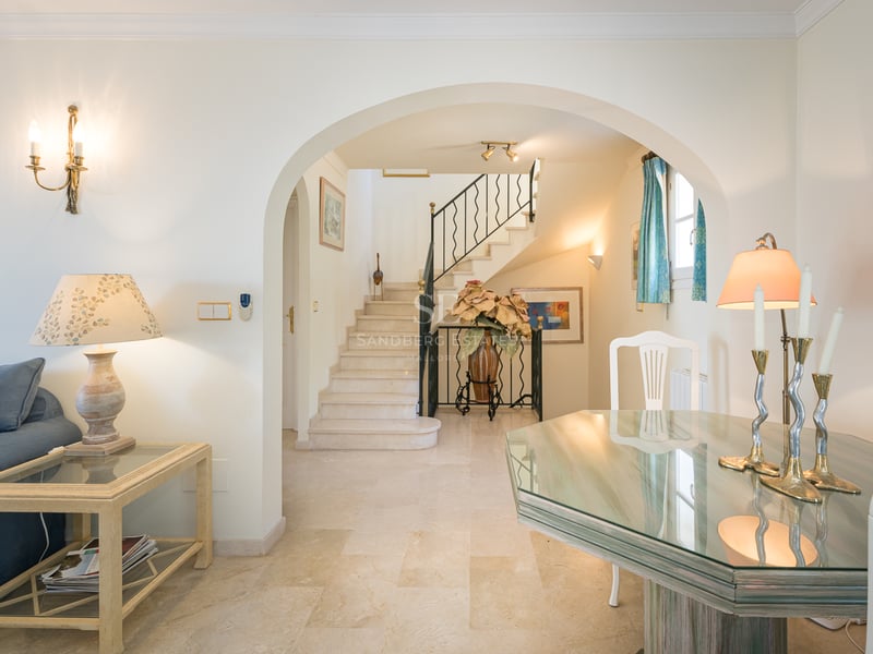Vue depuis un salon avec table en verre et canapé bleu vers une arche et un escalier en marbre.