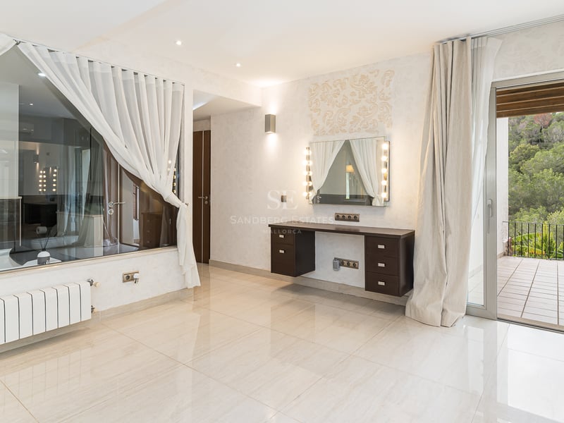 Espace dressing lumineux avec coiffeuse miroir Hollywood, paroi vitrée vers la salle de bain et terrasse vue forêt.