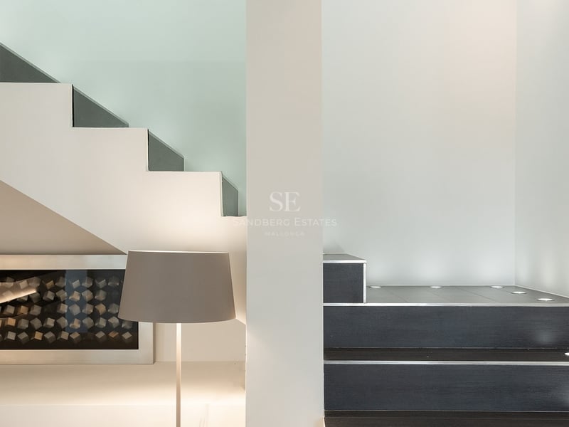 Gros plan d'un escalier minimaliste avec des marches sombres, des murs blancs et des spots LED encastrés au sol.