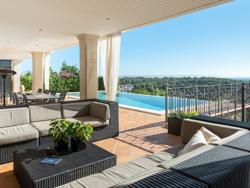 Terrasse de luxe ombragée avec canapés en osier, sol en terre cuite et piscine à débordement sur la mer.