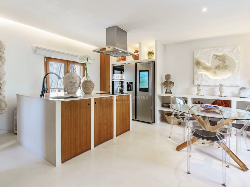 Cuisine moderne avec îlot en bois, appareils en acier inoxydable et table à manger en verre avec chaises transparentes.