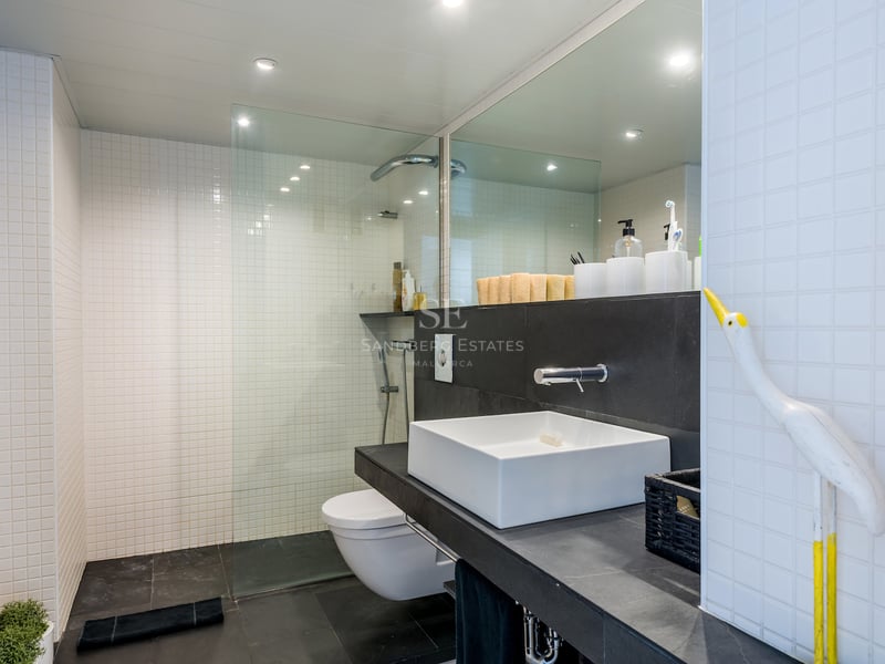 Salle de bain moderne avec carrelage blanc, sol noir, douche en verre et vasque carrée.