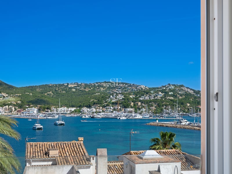 Vue d'un port méditerranéen rempli de yachts, d'eaux turquoise et de villas à flanc de colline sous un ciel bleu.