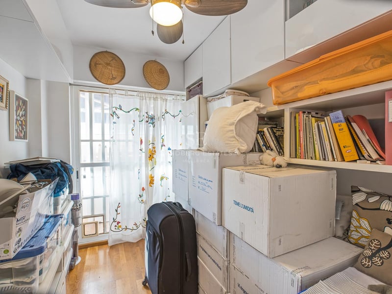 Petite pièce avec placards intégrés blancs, étagères, cartons de déménagement, ventilateur de plafond et fenêtre.