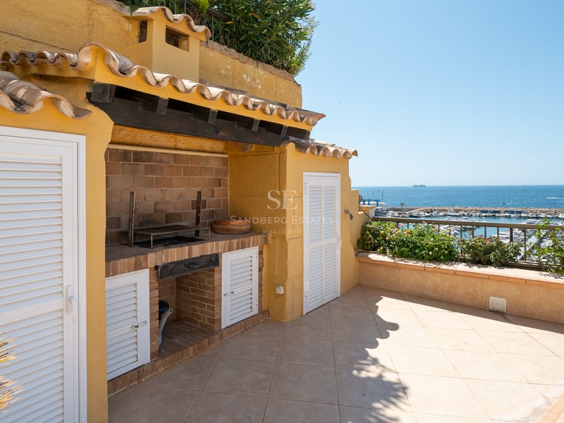 Terrasse extérieure avec barbecue en briques, murs jaunes et vue sur un port de plaisance et l'océan.