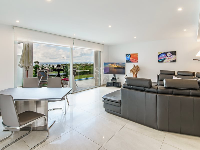 Salon moderne avec canapé en cuir gris foncé, coin repas et grandes baies vitrées ouvrant sur une vue mer.