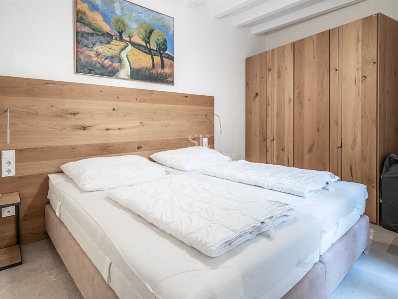 Chambre avec grande armoire en chêne, tête de lit en bois intégrée et lit double avec draps blancs.