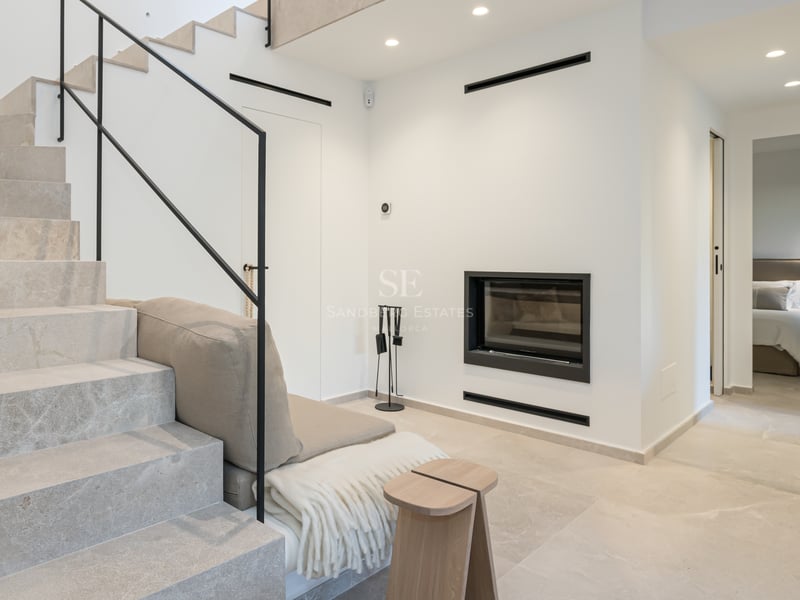 Intérieur moderne avec escalier en pierre claire, rampe noire minimaliste et cheminée murale intégrée.