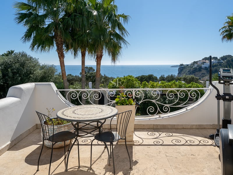 Terrasse blanche avec mobilier en fer et elliptique offrant une vue sur les palmiers et la mer Méditerranée.