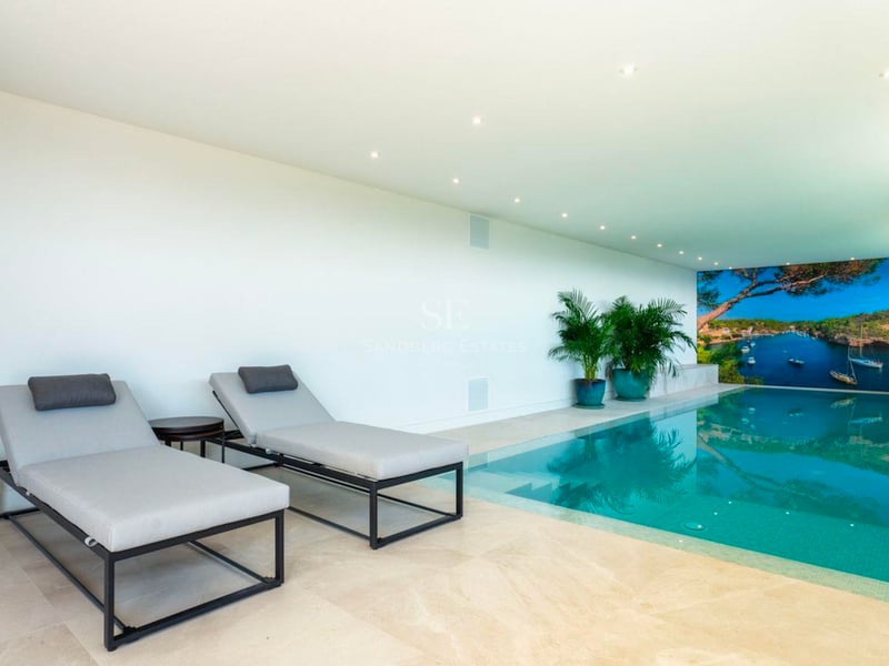 Piscine intérieure moderne avec eau turquoise, chaises longues grises et une grande murale côtière.