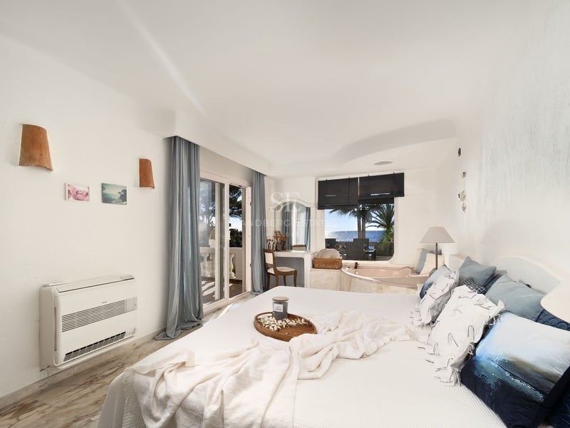Chambre principale blanche et lumineuse avec baignoire intégrée près de la fenêtre et balcon vue mer.