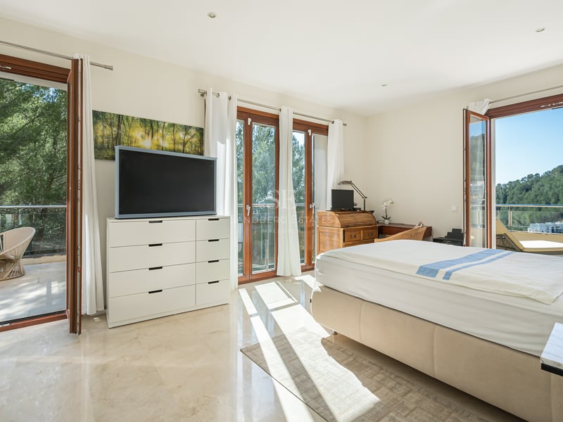 Chambre ensoleillée avec sol en marbre, lit double et portes vitrées ouvrant sur un balcon avec vue sur les collines.