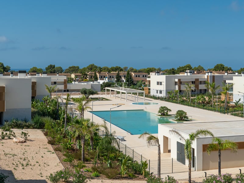 Vista elevada de una gran piscina turquesa rodeada de edificios modernos blancos y palmeras bajo un cielo azul.