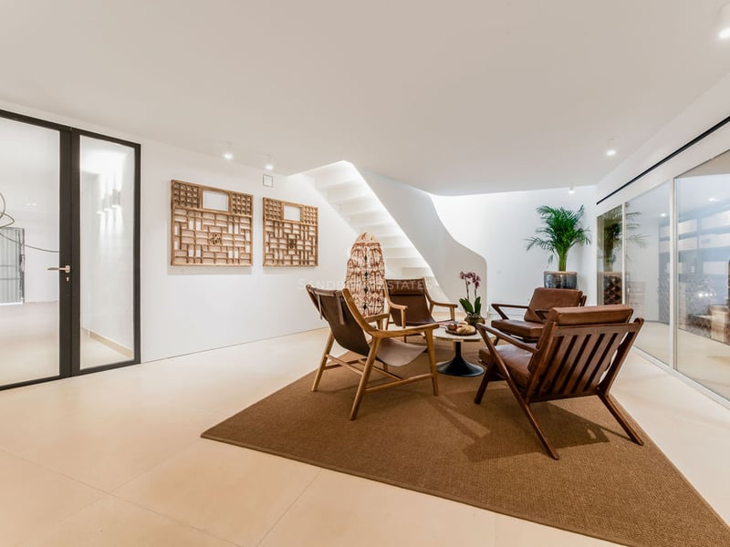 Espace salon moderne avec chaises en cuir, escalier blanc courbé et cave à vin vitrée en arrière-plan.