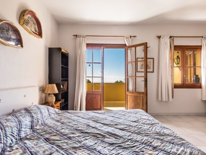 Chambre lumineuse avec des portes-fenêtres en bois ouvrant sur une vue mer, des murs blancs et une décoration traditionnelle.