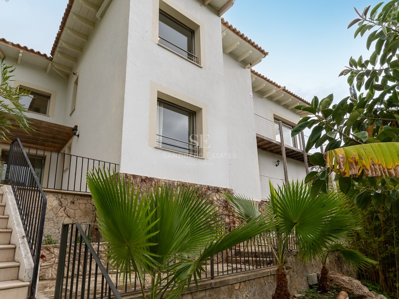 Façade de villa blanche avec soubassement en pierre, escaliers extérieurs et palmiers sous un ciel dégagé.