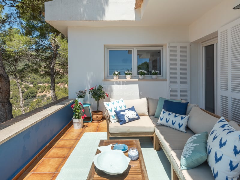 Terrasse extérieure avec un grand canapé en L, des coussins bleus et une table en bois surplombant une vallée de pins.