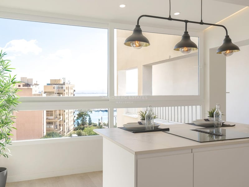 Îlot de cuisine blanc avec plaque de cuisson devant une fenêtre offrant une vue sur le port et la ville.