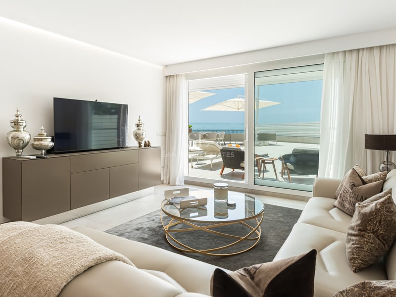 Salon moderne avec canapés en cuir crème, table basse ronde en verre et baies vitrées ouvrant sur une terrasse.