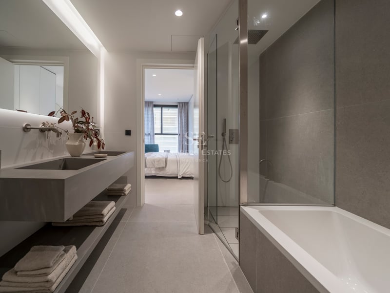 Salle de bain contemporaine avec double vasque grise, douche vitrée, baignoire et vue sur la chambre.