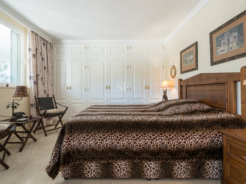 Chambre avec un lit imprimé léopard, des meubles en bois sombre et un mur de placards blancs intégrés.