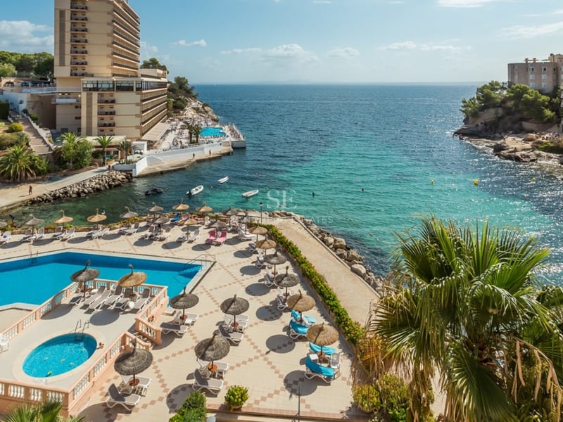 Vue aérienne d'une piscine avec chaises longues et parasols surplombant une baie turquoise et une côte rocheuse.