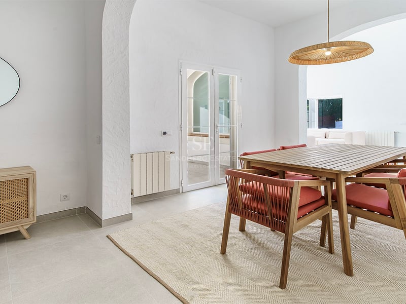 Salle à manger lumineuse avec table en bois, chaises terre cuite, luminaire en osier et arches blanches.