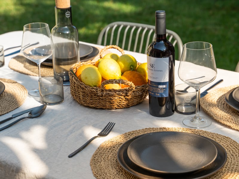 Table de salle à manger extérieure dressée avec du lin, de la vaisselle noire, du vin de Majorque et des citrons.