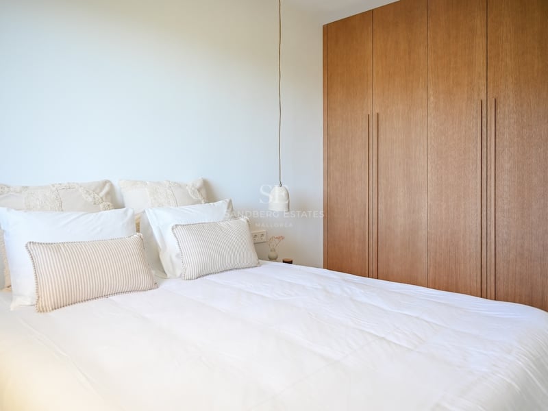 Chambre lumineuse avec lit blanc, coussins rayés et grands placards intégrés en bois du sol au plafond.