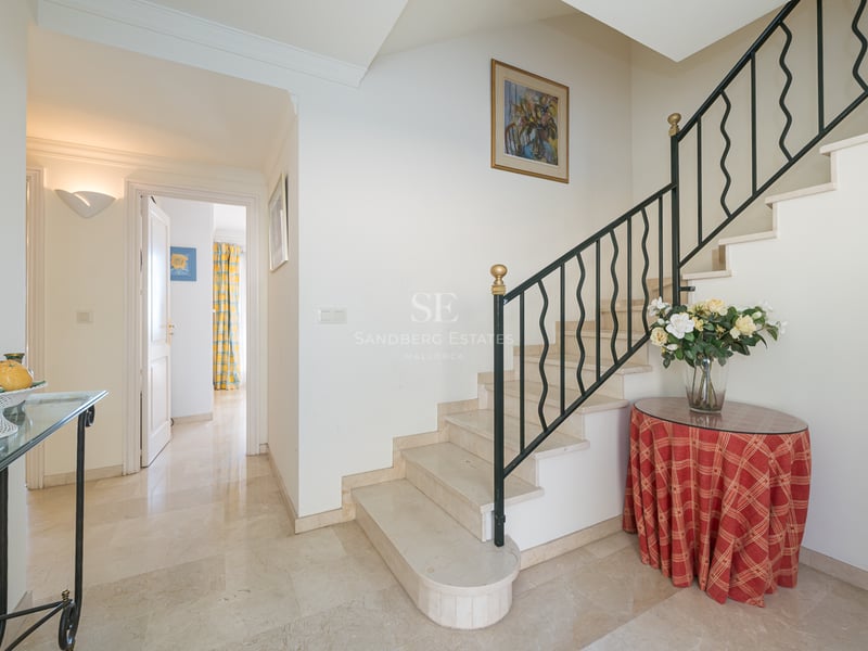 Hall d'entrée lumineux avec escalier en marbre crème, rampe en fer forgé et sol en pierre polie.