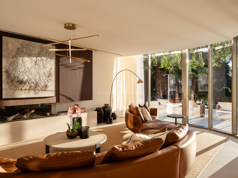 Salon moderne avec canapé en cuir courbé, cheminée linéaire et baies vitrées donnant sur le jardin.