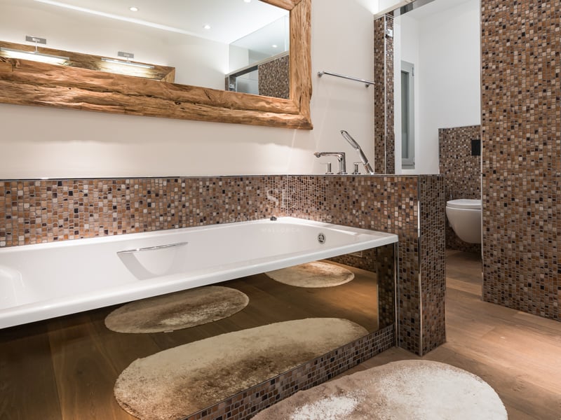 Baignoire blanche moderne avec base en miroir, mur en mosaïque marron et grand miroir avec cadre en bois brut.