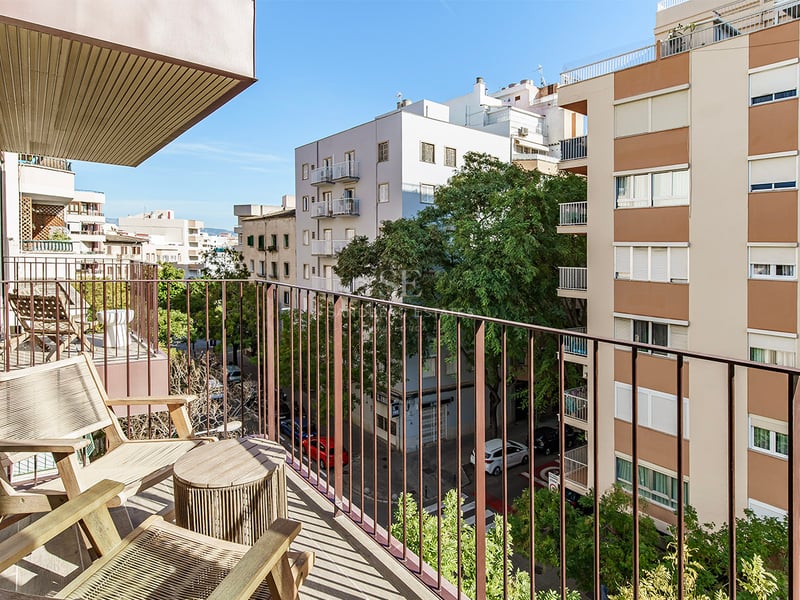 Balcon avec chaises longues en bois offrant une vue sur une rue urbaine avec des arbres et des bâtiments modernes.