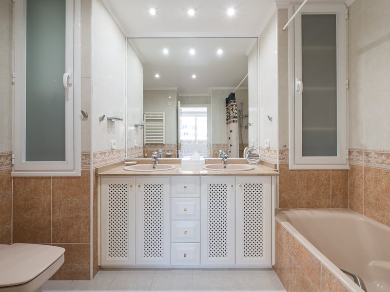 Grande salle de bain avec deux lavabos, grand miroir, baignoire et bidet dans les tons beige et terre cuite.