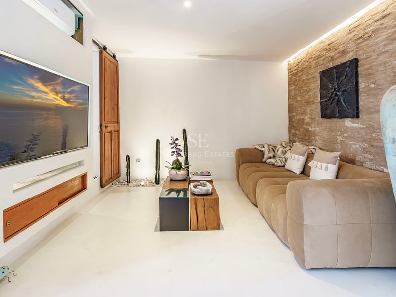 Salon avec canapé beige, mur en pierre rustique, télévision encastrée et décoration méditerranéenne.