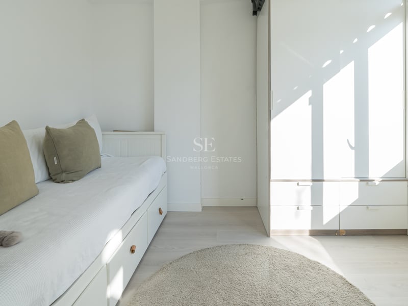 Chambre blanche avec lit gigogne, coussins vert olive, grande armoire et tapis rond gris.