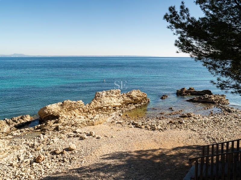 Vue surélevée d'une crique rocheuse méditerranéenne aux eaux turquoises et horizon dégagé sous un ciel bleu.