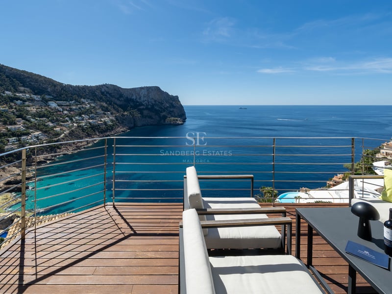 Terrasse en bois surélevée avec salon d'extérieur surplombant une baie méditerranéenne.