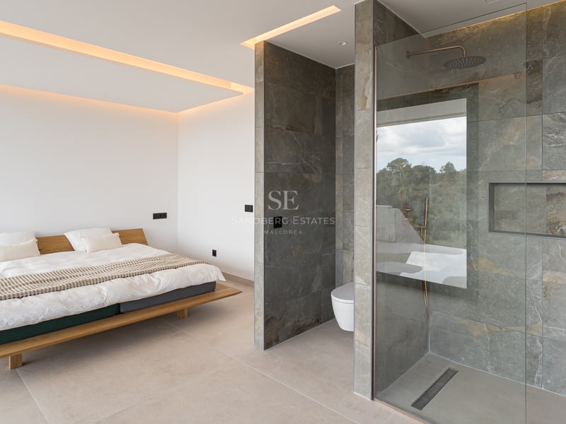 Chambre moderne avec lit flottant en bois et salle de bain ouverte avec carrelage en pierre grise et douche vitrée.