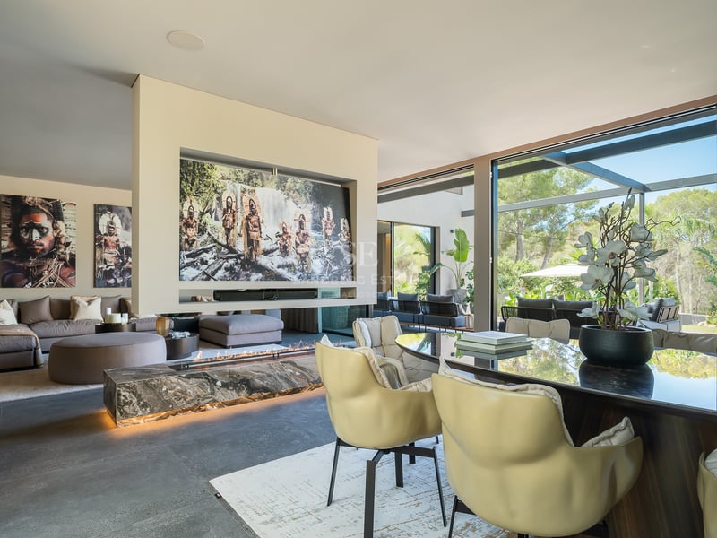 Salon de luxe à aire ouverte avec cheminée en marbre, mobilier moderne et baies vitrées sur le jardin.