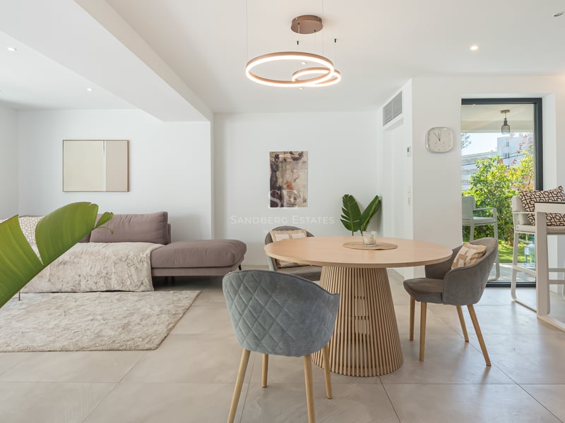 Séjour moderne avec table à manger ronde en chêne, chaises grises et vue sur une terrasse verdoyante.