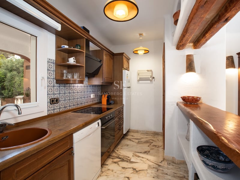 Cuisine étroite avec meubles en bois sombre, sol en marbre, poutres apparentes et crédence en carreaux de ciment.