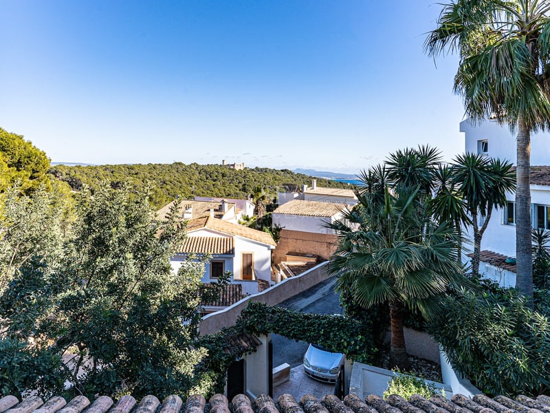 Vue panoramique en hauteur montrant des villas blanches, une végétation luxuriante, un château au loin et la mer.
