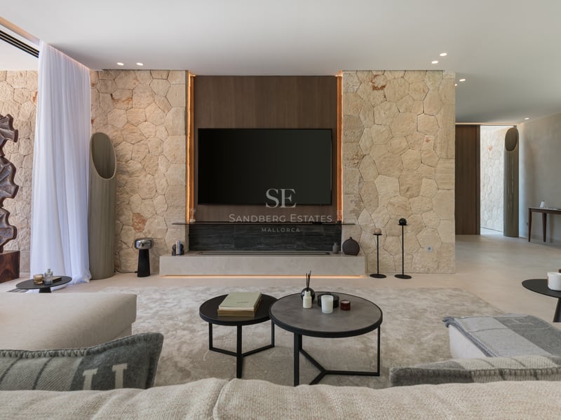 Salon moderne avec mur en pierre naturelle, meuble TV intégré et mobilier minimaliste aux tons neutres.