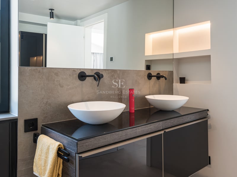 Salle de bains contemporaine avec deux vasques blanches, robinetterie murale noire mate et éclairage d'ambiance.