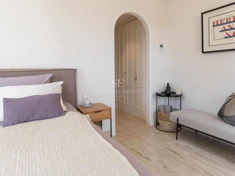 Chambre moderne avec lit rembourré mauve, sol en marbre travertin et arche menant au dressing.