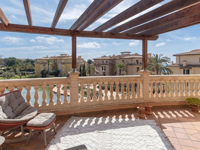 Terrasse ensoleillée avec pergola en bois, balustrade en pierre et tapis extérieur donnant sur des palmiers.
